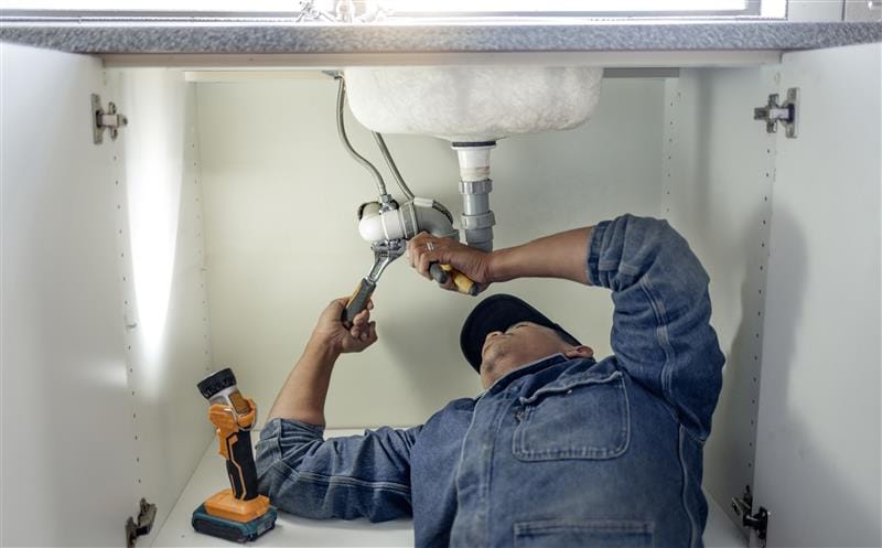Plumber repairing pipes beneath a bathroom sink in Gilroy
