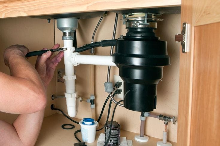Plumber installing a garbage disposal beneath a kitchen sink in Gilroy