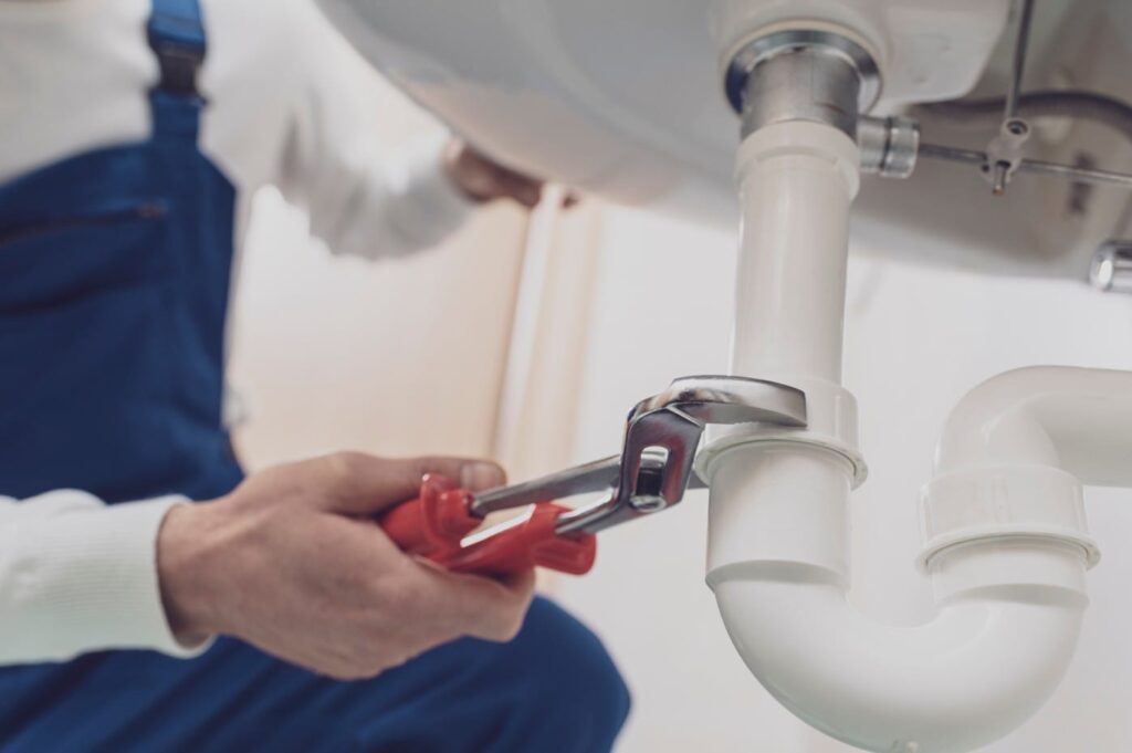Plumber repairing a white drain pipe beneath a sink in Gilroy