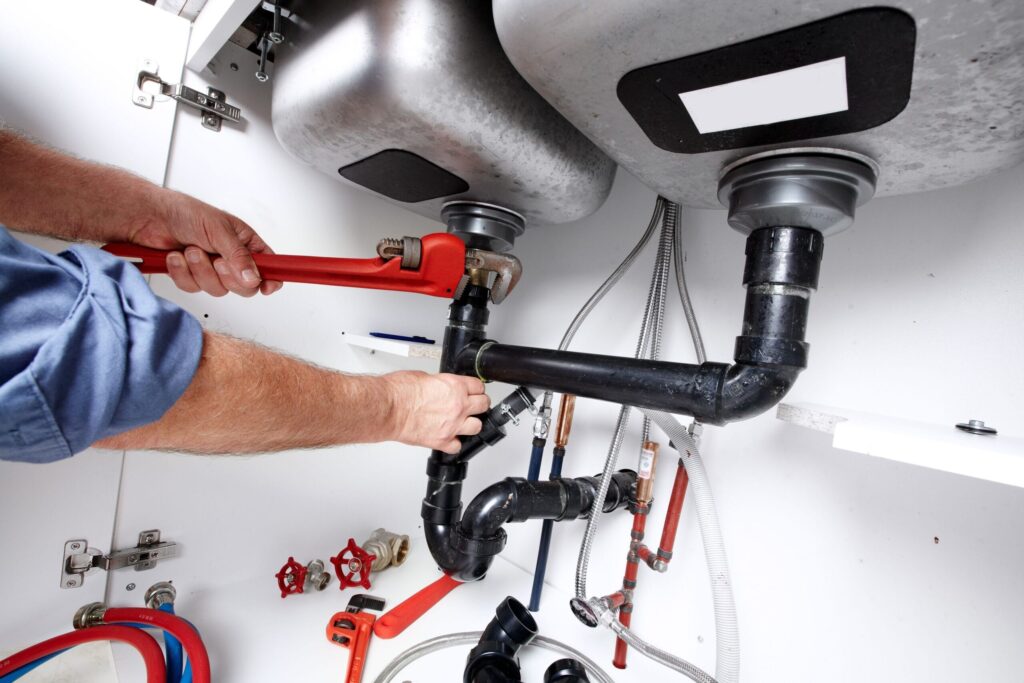 Plumber repairing drain pipes beneath a kitchen sink in Gilroy